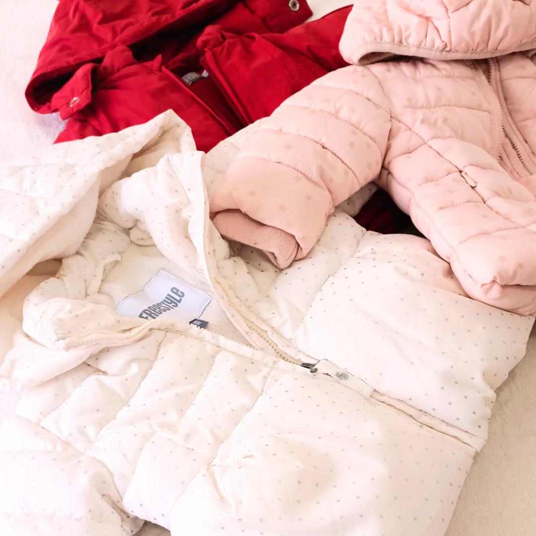 Vista superior de tres anoraks de bebé: rojo de Boboli, rosa con estrellas doradas y blanco con estrellitas grises de Freestyle, perfectos para el invierno.