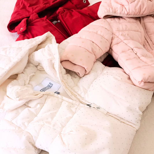 Vista superior de tres anoraks de bebé: rojo de Boboli, rosa con estrellas doradas y blanco con estrellitas grises de Freestyle, perfectos para el invierno.