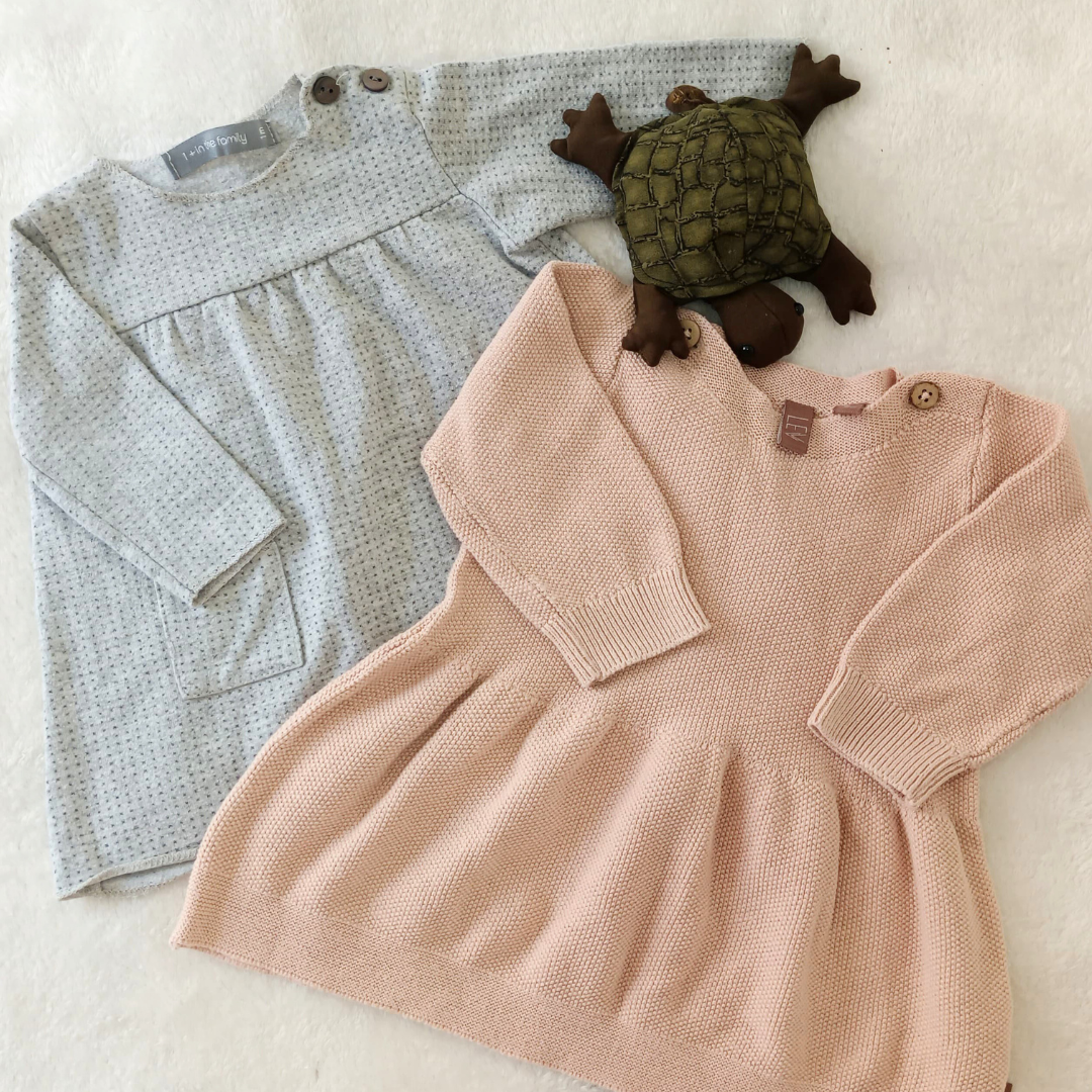 Pack de dos vestidos para bebé: uno de punto rosa de la marca Levv y otro gris jaspeado de la marca 1+ in the Family, presentados sobre fondo blanco.