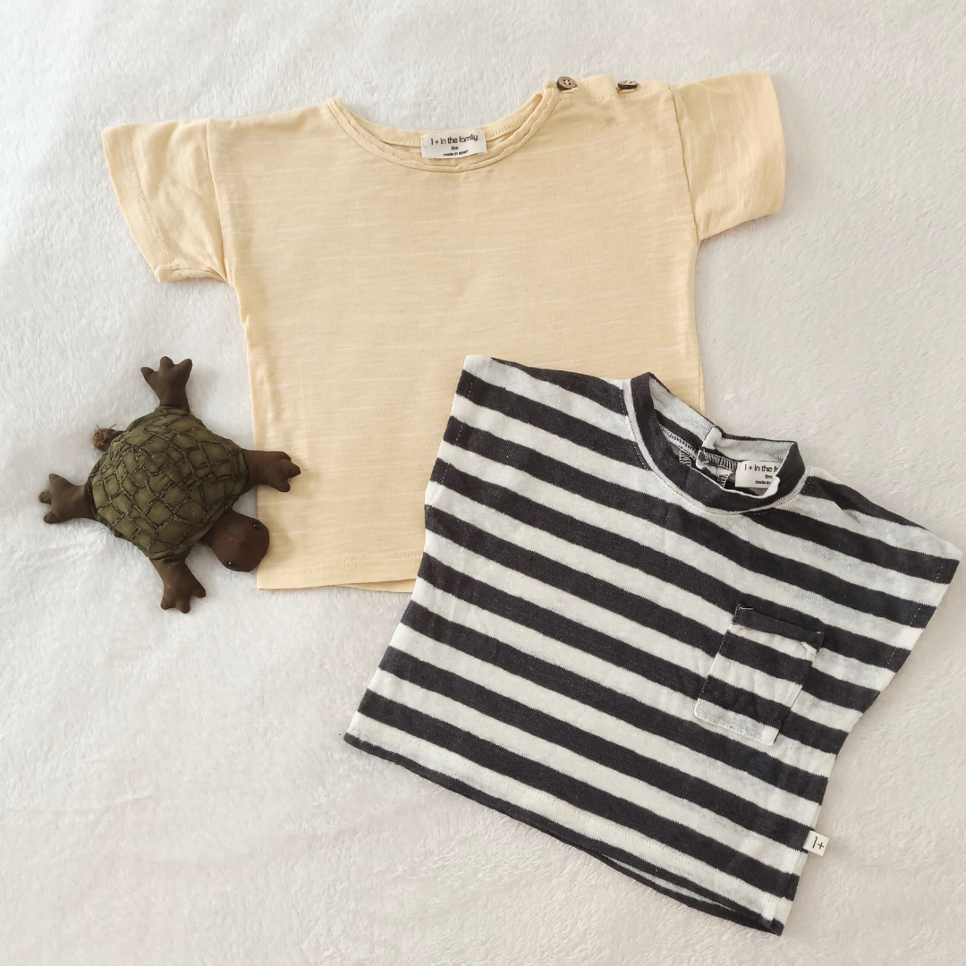 Pack de dos camisetas de bebé marca 1+ in the Family, una de rayas negras y blancas con bolsillo y otra en color beige liso con botones en el hombro.