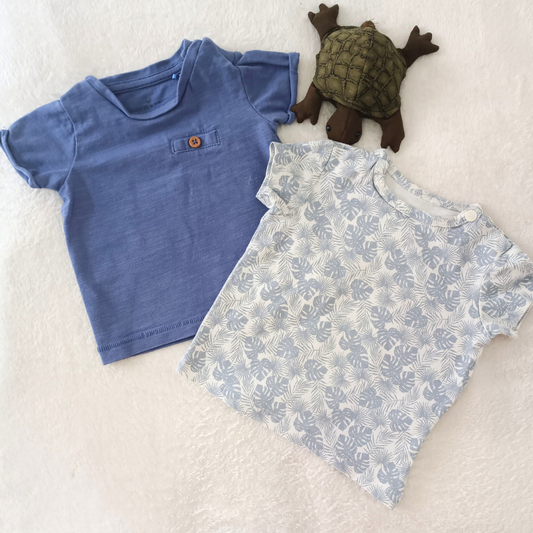 Pack de dos camisetas de bebé marca Cuddle & Smile, una azul lisa con bolsillo decorativo y otra blanca con estampado tropical azul claro.